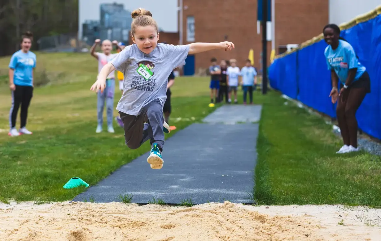 Young student mid-leap in a long jump activity during a physical education class at Trinity School, displaying the energy and enthusiasm for sports in the Lower School program.