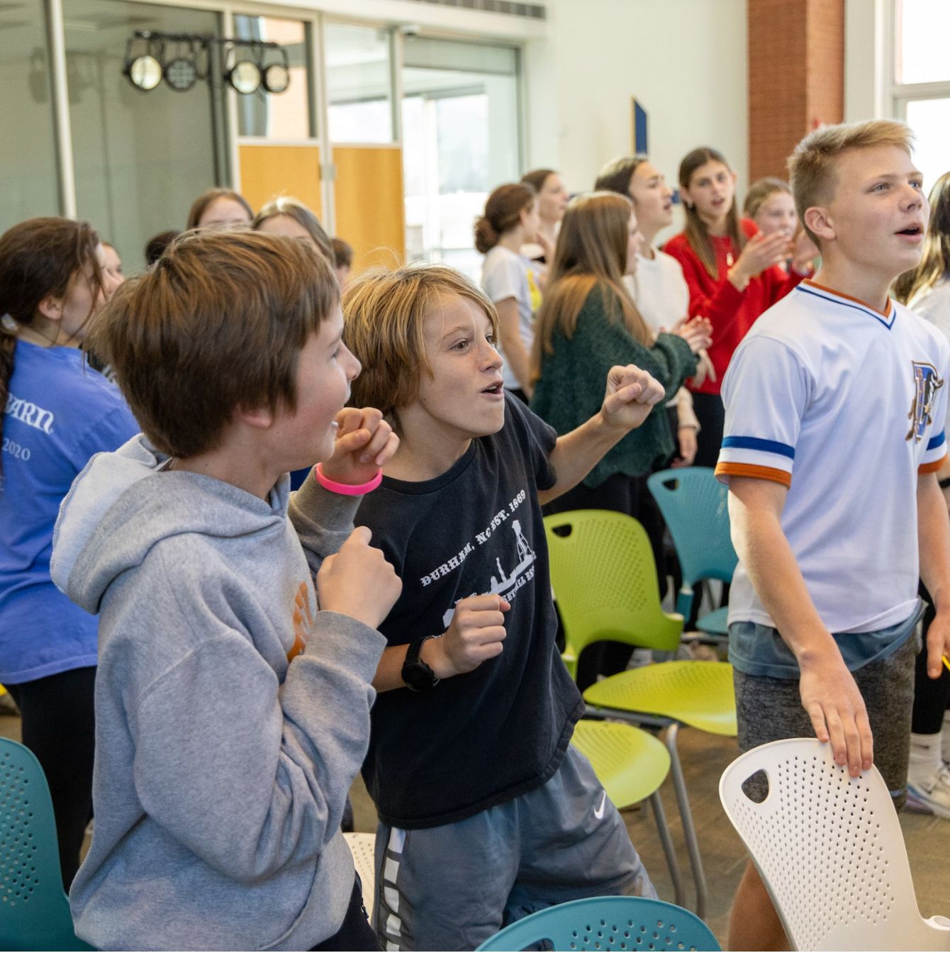 A group of middle school students are caught in a moment of excitement and anticipation at a school event, with expressions of joy and engagement on their faces.