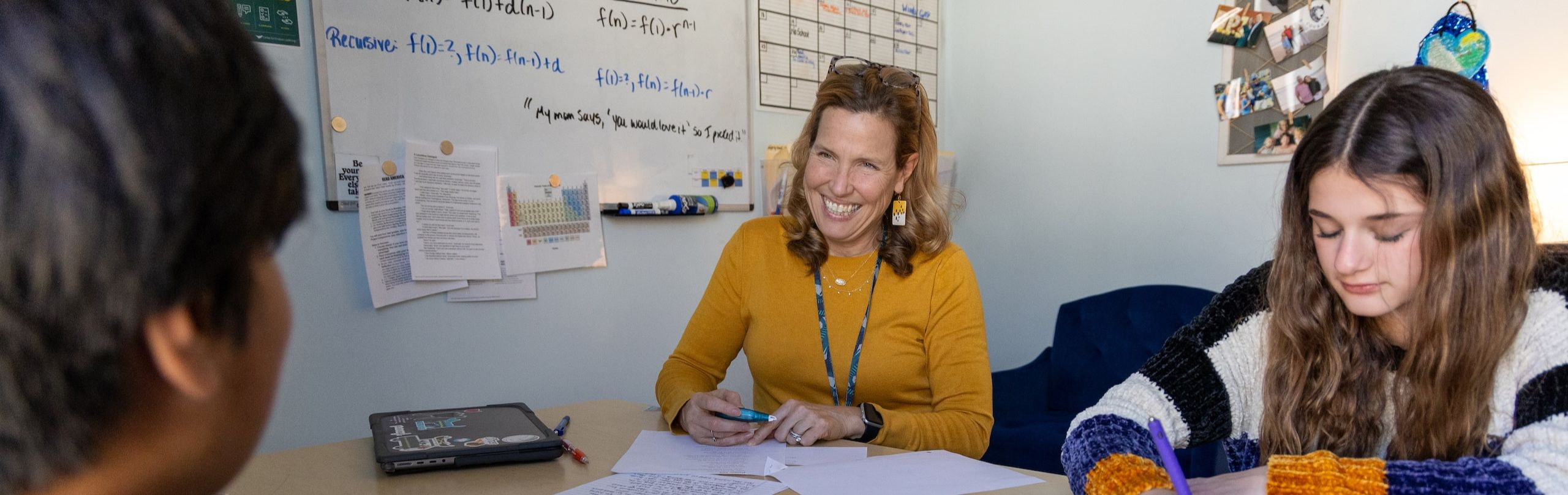 A middle school teacher provides personalized attention to students during a tutoring session in a well-organized classroom, highlighting the value of individualized education.