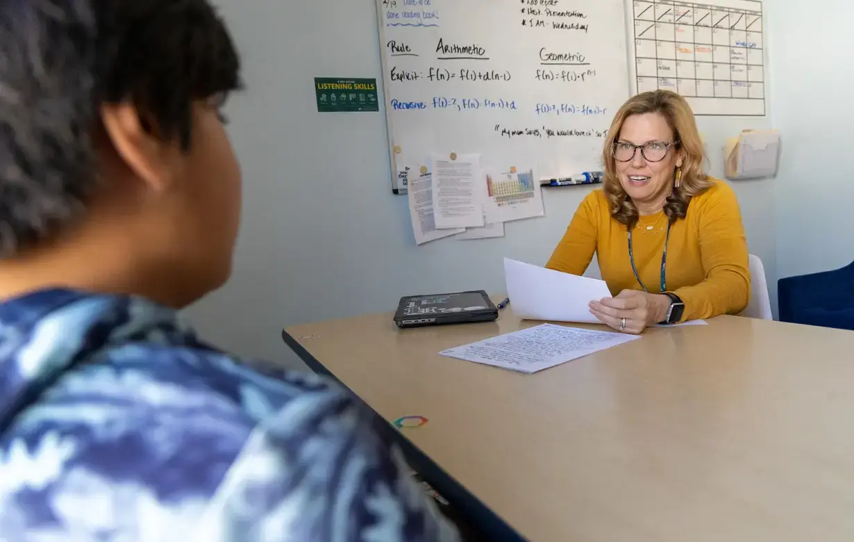 A middle school teacher provides personalized attention to students during a tutoring session in a well-organized classroom, highlighting the value of individualized education.