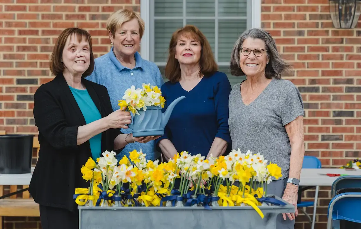 Four mothers stand in a line in front of a flower box full of daffodils smiling