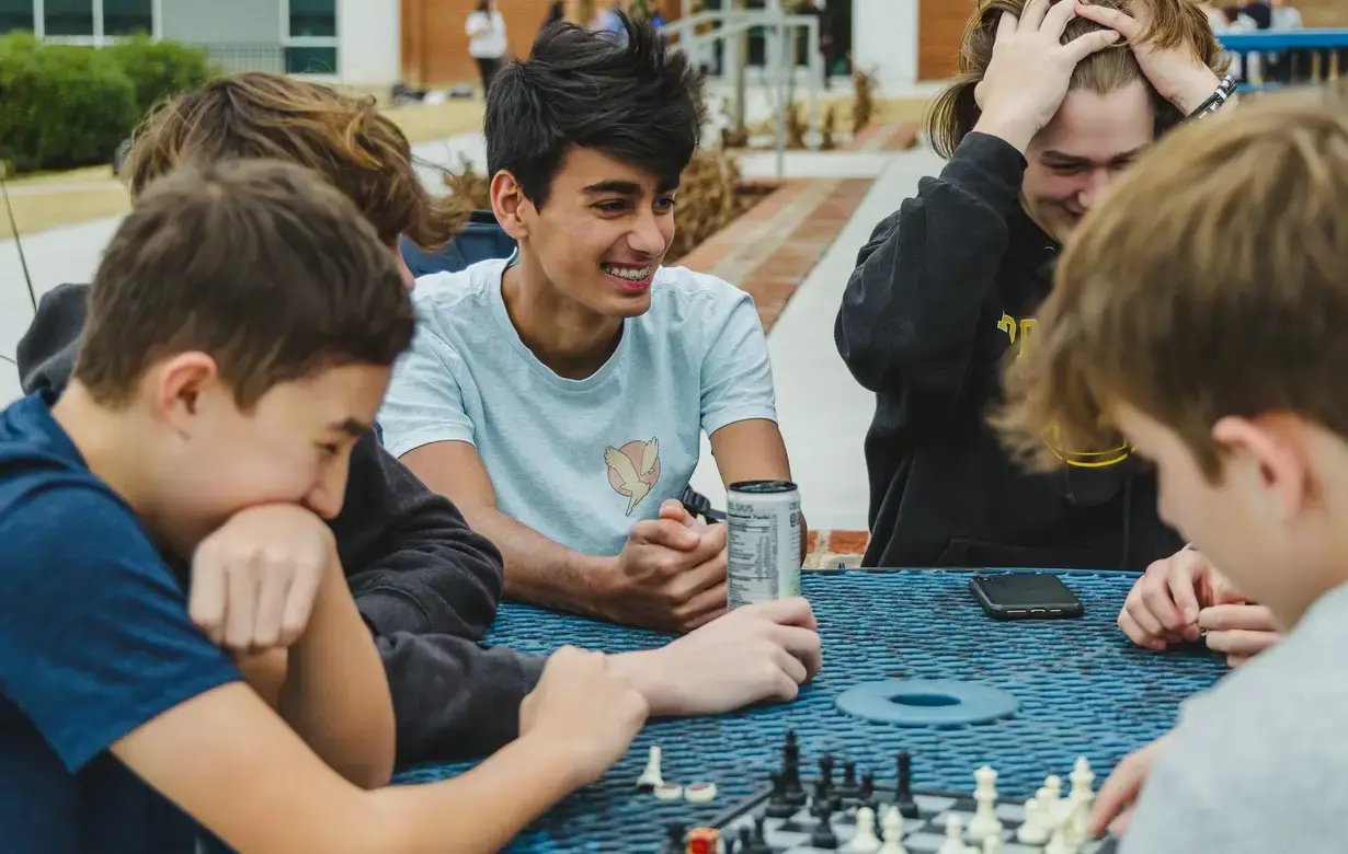 Group of male students laughing and playing chess outside