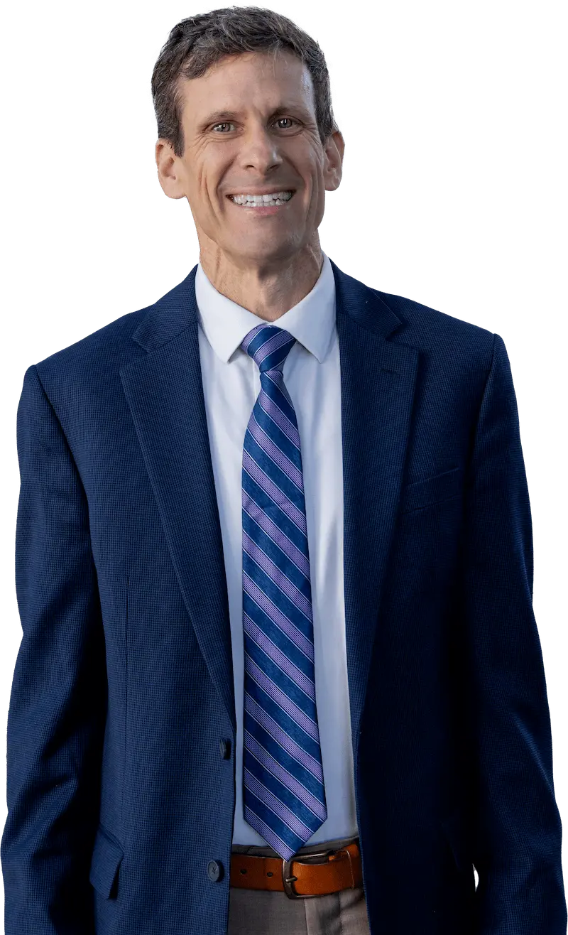 A professional headshot of an educator smiling confidently, dressed in a sharp blue suit and striped tie, standing in a well-lit space.