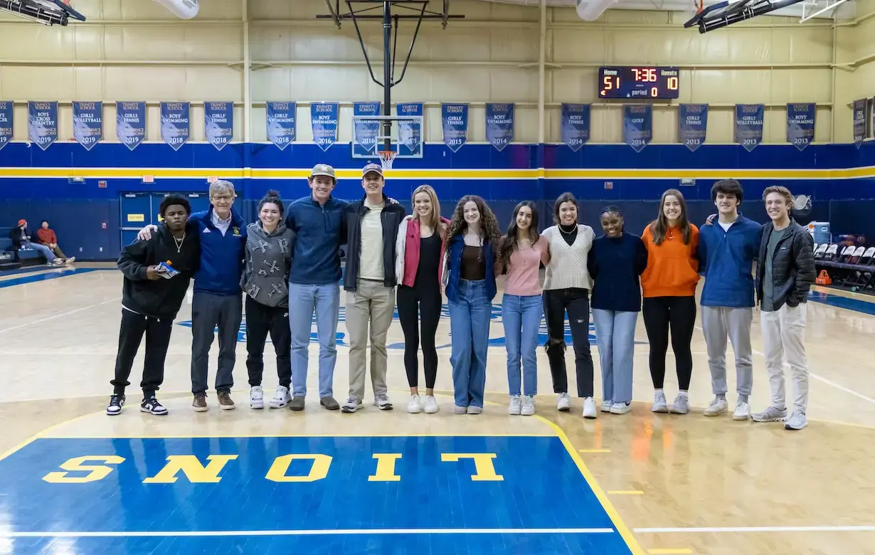 Alumni students stand on the basketball court arm in arm