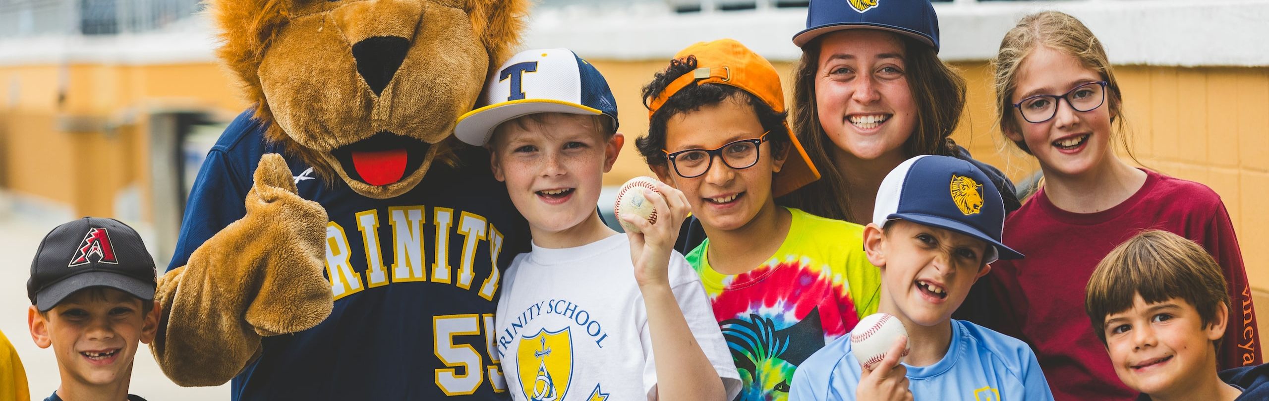 Group of Lower School Trinity students holding baseballs with Trinity Lions mascot