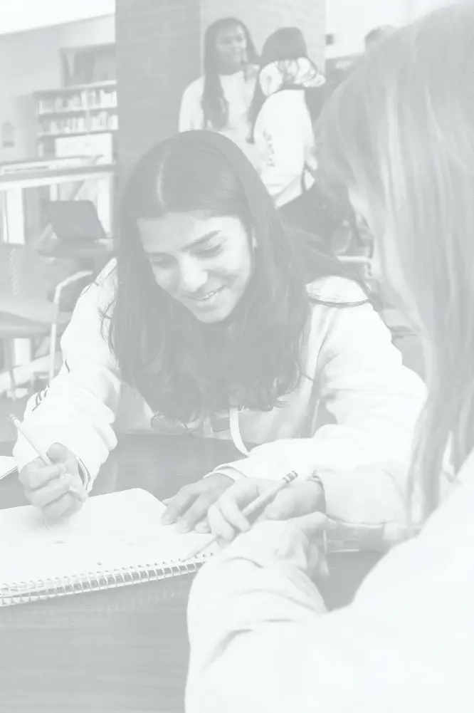 An engaging study session in the library with a teacher and two students smiling and discussing over notebooks.