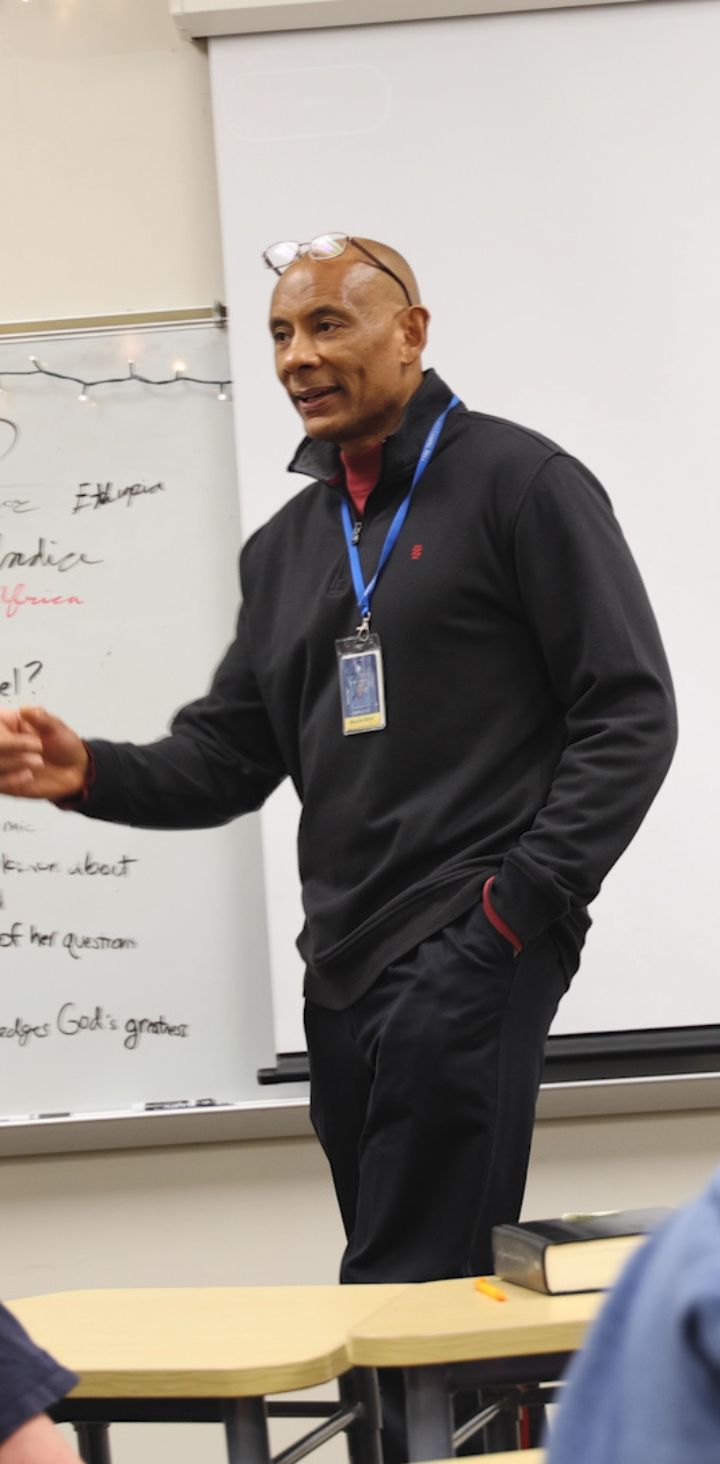 An animated teacher engaging with students during a classroom lesson, with a whiteboard in the background filled with notes on biblical themes.